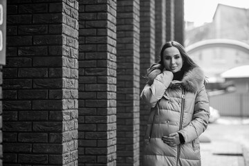Fototapeta premium Beautiful young pregnant woman in a brown coat, in the background a brick wall
