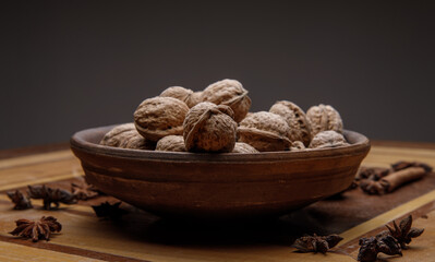 Nuts. whole walnuts in an earthenware dish on a dark wooden table near cinnamon and star anise. selective soft focus.