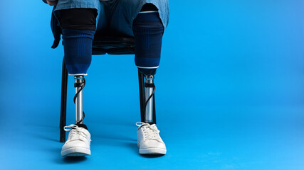 View of a man with prosthetic legs and white sneakers sitting on a chair, blue background