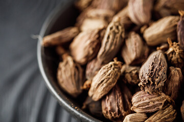 a barrel of dried black cardamom on a black wooden rustic background