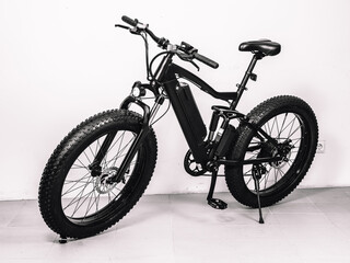 Modern black bicycle with thick wheels and an electric motor. White wall.
