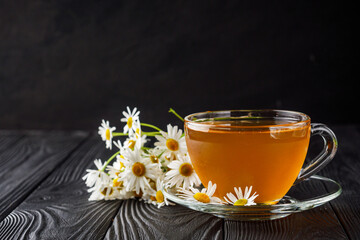 aromatic hot chamomile tea on a black rustic wooden background