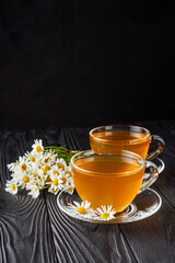 aromatic hot chamomile tea on a black rustic wooden background