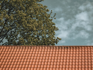 Red tiled roof. CLouds in blue sky. Green tree. Spring or summer nature.