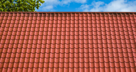 Red tiled roof. CLouds in blue sky. Green tree. Spring or summer nature.