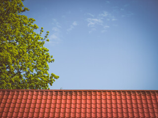Red tiled roof. CLouds in blue sky. Green tree. Spring or summer nature.