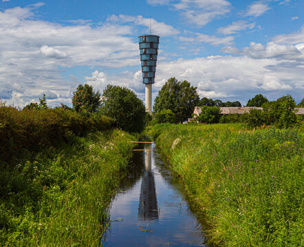 Modern urban architecture. Water tower. Reflection in water. Green grass and bushes. Sunny day.