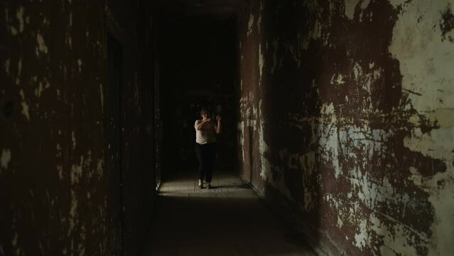 Overweight young woman have fun dancing in dark corridor of abandoned building. Person dances among shabby worn walls. Concept of success, joy in midst of life difficulties, winning inheritance.