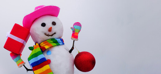 Christmas and winter fashion. Smiling snowman in hat, scarf and mittens with gift and New Year ball.