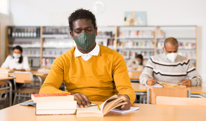 Fototapeta premium Portrait of African American adult in protective face mask visiting public library during coronavirus pandemic. Concept of compelled precautions..