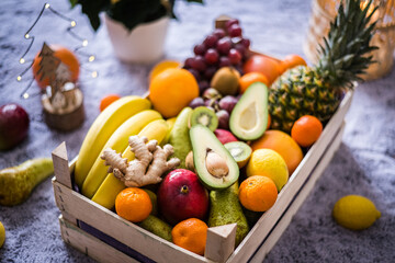 Winter healthy fruit wooden box with apples, kiwi, banana, avocado, ginger, pineapple, lemons, oranges and more ready for Christmass table.
