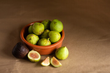 top view of figs in a clay bowl and figs cut in half on a light brown background