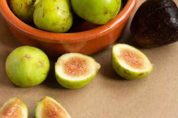 figs cut in half and figs in clay bowl on light brown background - close-up