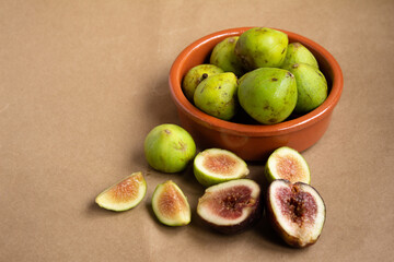 clay bowl with fresh figs and cut pieces - halves of figs - on a light brown background
