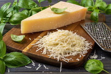 Shredded parmesan cheese and grater on a cutting board. Grana padano cheese whole wedge and grated,...