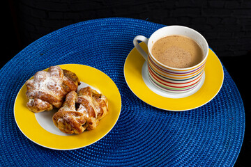 Mini sweet brioches topped with cinnamon powder and grated coconut on a dish and a mug of latte for a breakfast. Selective focus.