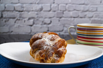 Mini sweet brioches topped with cinnamon powder and grated coconut on a dish and a mug of latte for a breakfast. Selective focus.