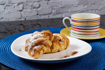 Mini sweet brioches topped with cinnamon powder and grated coconut on a dish and a mug of latte for a breakfast. Selective focus.