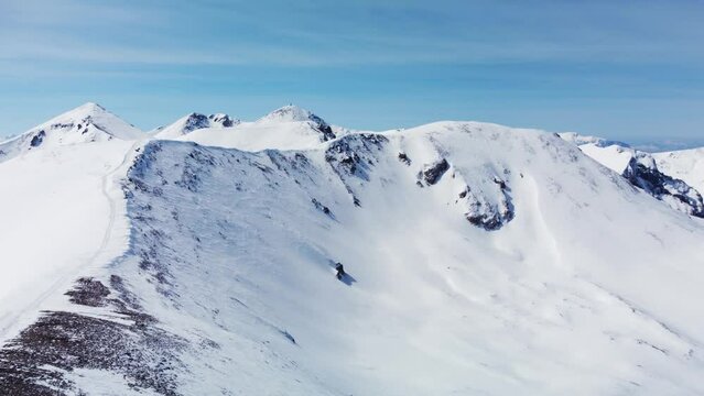 Aerial view of a mountain slope used for freeride skiing. Visible snowcat tracks on the egde and summit.