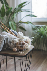 Cozy homely atmosphere. Female hobby knitting. Yarn in neutral colors in a white iron wire basket.