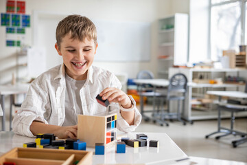 Happy male kid assembling Montessori material trinomial cube at school classroom desk