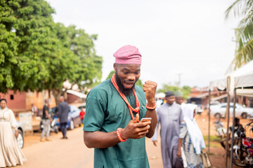 young African man excited looking at mobile at hand standing outside a rural street