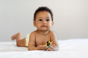 Fototapeta na wymiar Portrait Of Cute Little Black Baby Lying In Bed On His Tummy