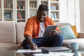 Black businessman sitting at home, looking at screen of tablet