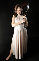 Beautiful pregnant woman in the dress posing with the acoustic guitar isolated on the black - 553610841