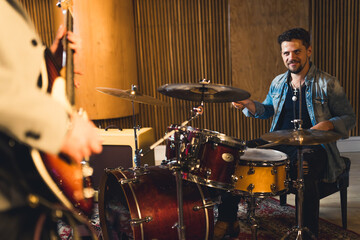 full shot of a young drummer sitting and playing drums with his band in the studio. High quality photo