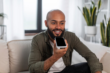 Portrait of positive latin man holding cellphone near mouth recording message talking on smartphone