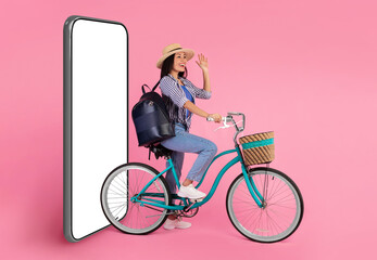 Excited asian woman riding bicycle waving hand, smartphone with mockup