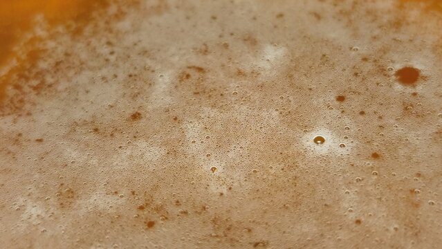 Amber beer in a glass. Light brown beer is in a round thin transparent glass. On top is a small even white layer of foam. Foam consists of many small round bubbles.