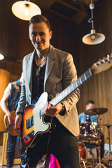 Fototapeta premium medium-full shot of a nice-looking young guitarist playing on repetition with his band, indoor music studio. High quality photo