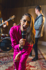 vertical medium-full shot of a young soloist singing and performing with her band in a studio. High quality photo