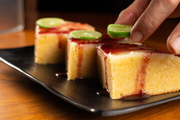 three pieces of lemon brownie with blackberry jam marmalade cover with a lemon slice on a square black plate dish, dark food photo