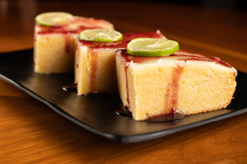 three pieces of lemon brownie with blackberry jam marmalade cover on a square black plate dish, dark food photo