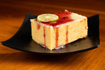 single piece of lemon brownie with blackberry jam marmalade cover on a square black plate dish, dark food photo