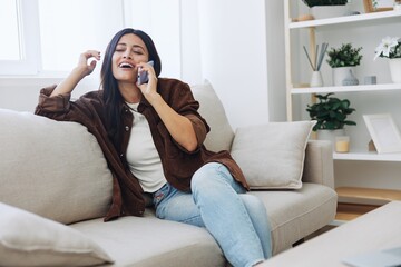 Woman blogger with phone lying at home and talking on the phone on sofa with laptop and working freelancer online, selfie