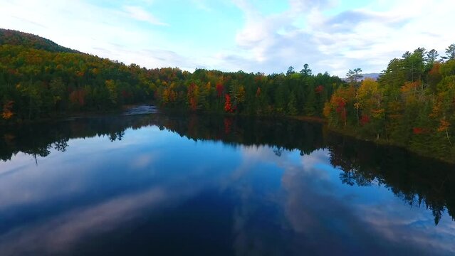 Aerial over mountains in peak fall surround reflective lake in early morning light