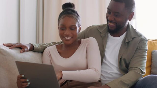 Young happy african american couple web surfing online on digital tablet at home and discussing content, free space