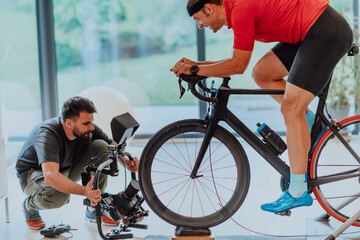 A cameraman filming an athlete riding a triathlon bike on a simulation machine in a modern living...