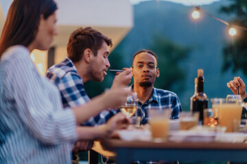 A group of young diverse people having dinner on the terrace of a modern house in the evening. Fun for friends and family. Celebration of holidays, weddings with barbecue.