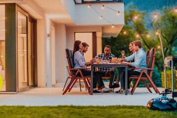 A group of young diverse people having dinner on the terrace of a modern house in the evening. Fun...