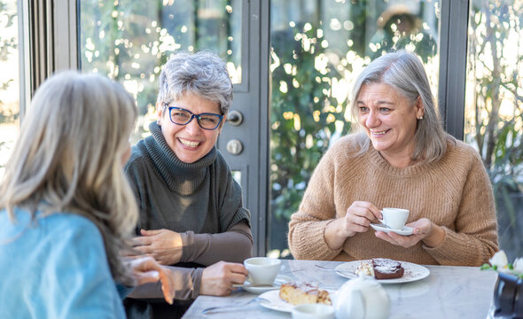 Group of smiling mature women having breakfast together. Three senior female friends laugh together