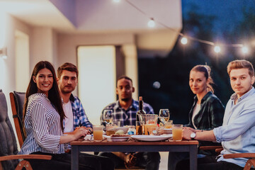 A group of young diverse people having dinner on the terrace of a modern house in the evening. Fun for friends and family. Celebration of holidays, weddings with barbecue.