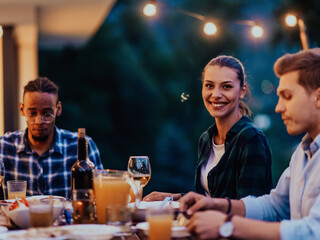 A group of young diverse people having dinner on the terrace of a modern house in the evening. Fun for friends and family. Celebration of holidays, weddings with barbecue.