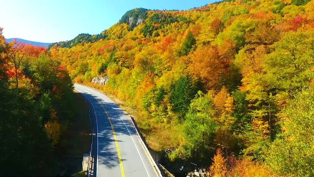 Aerial low to high from stunning road through New Hampshire to wide view of mountains during peak fall foliage