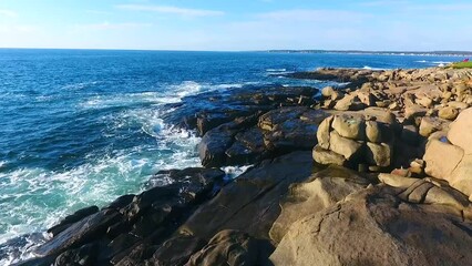 Aerial across Rocky coasts of Maine with ocean waves crashing into cliffs