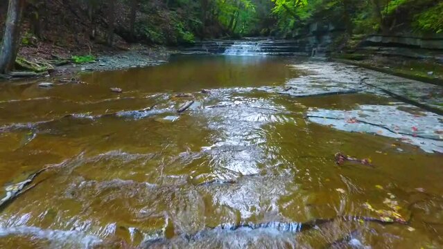 Low aerial backwards over river towards walking path along gorge with pair of waterfalls in Upstate New York